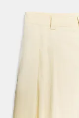 Bermudas de tiro medio color amarillo claro, confeccionadas en mezcla de algodón. Presentan cintura con trabillas, bolsillos laterales ocultos en costura, pliegues delanteros y cierre frontal con cremallera, botón y ganchos metálicos.