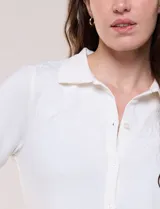 Camisa blanca de manga corta con cuello solapa, cierre frontal de botones, detalles bordados al tono en el pecho y lazos para anudar en las mangas.