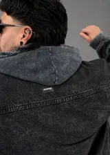 Chaqueta de denim negro con lavado ácido, cuello mao, mangas cortas, cierre frontal con botones metálicos y un bolsillo aplicado en el pecho. Presenta detalles de terminaciones desflecadas en el cuello, mangas y ruedo.