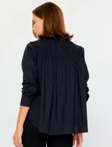 Camisa blanca de manga larga con cuello clásico y cierre frontal de botones. Presenta detalles bordados florales tono sobre tono en la zona de los hombros y el pecho.