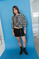 Blusa estampada en blanco y negro, con cuello redondo y mangas globo de puños elastizados largos. Presenta tiras ajustables en los laterales.