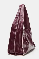 Bolso tipo shopper en formato horizontal, de efecto acharolado en color bordó con detalles de pespuntes en contraste. Cuenta con asa ancha de hombro, bolsillo interior con cierre y cierre principal con botón imantado.