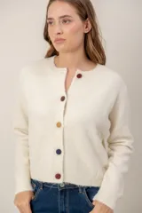 Cardigan de punto color crema con cuello redondo, manga larga y cierre frontal con botones forrados de distintos colores.