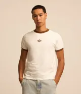 Remera estilo baby tee de color blanco, confeccionada en algodón, con cuello redondo y ribetes en color marrón en cuello y puños. Cuenta con un pequeño tag gomosa con el logotipo "Lucky" en el centro del pecho.