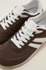Zapatillas de estilo urbano color marrón con detalles en blanco, confeccionadas en material textil y sintético, con cordones blancos y suela de goma.