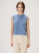 Musculosa crop de algodón color celeste con efecto acid wash, cuello redondo, hombreras marcadas y pequeño gráfico bordado en el centro del pecho. Presenta costuras con pespuntes en color rosa contrastante.