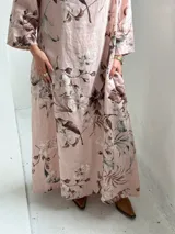 Vestido largo rosado con estampado floral en tonos marrones y beige, cuello drapeado y mangas largas holgadas.