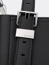Cartera tipo tote de tamaño compacto, confeccionada en piel sintética lisa color negro. Presenta doble asa de mano ajustable con detalle de hebilla metálica y correa larga ajustable. Incluye cierre principal con cremallera y logo de la marca grabado en la parte inferior frontal.
