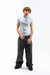 Pantalón de denim azul desgastado, corte mega baggy con piernas anchas y bolsillos traseros grandes. Presenta un bordado dorado en estilo gótico en el bolsillo trasero izquierdo.