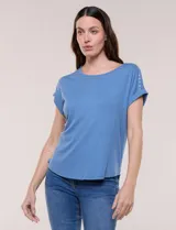 Remera de tejido de punto acanalado color celeste, con escote a la base decorado con tachas metálicas en el cuello y los hombros, mangas cortas estilo japonesa con dobladillo y ruedo curvo.