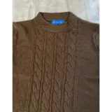 Sweater de punto color blanco marfil, con diseño de trenzas frontales, cuello redondo y mangas largas con puños elásticos acanalados.