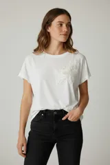 Remera de algodón blanca con cuello redondo y detalle de aplique floral en relieve sobre el pecho.
