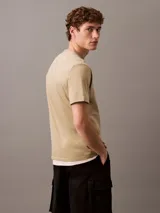 Remera de algodón con cuello redondo y manga corta, color beige. Presenta un estampado frontal con el logo de Calvin Klein y la inscripción New York en estilo cursivo.