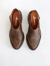 Zapato tipo zueco de cuero color chocolate con efecto desgastado, plataforma y taco cuadrado. Presenta una tira trasera ajustable con hebilla metálica.