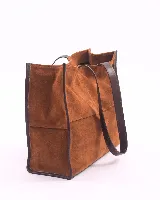 Bolso tipo shopper de gran tamaño, confeccionado en cuero gamuzado color marrón. Presenta estructura rectangular con bordes reforzados en cuero liso oscuro, doble asa de hombro y cierre mediante botón magnético.