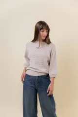 Buzo de tejido liviano en color beige, con diseño calado de líneas horizontales, cuello redondo y mangas largas levemente abullonadas con terminaciones en rib.