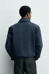 Cazadora boxy fit color azul marino, confeccionada en tejido de algodón. Presenta cuello solapa, manga larga con puño abotonado, bolsillos de vivo en la cadera y bajo elástico. Cierre frontal con cremallera.