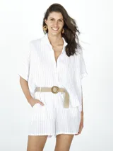 Camisa blanca con finas rayas verticales grises, de lino y corte holgado, con cuello clásico, cierre frontal con botones y mangas cortas caídas. Incluye cinturón de soga con hebilla redonda de madera.