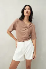 Remera blanca de manga corta con escote asimétrico y detalle de nudo con frunces en el centro del busto.