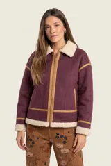 Campera tipo gamulán de color bordó, con interior y cuello de corderito sintético en tono crema. Presenta detalles de ribetes en cuero sintético color suela, cierre frontal metálico y bolsillos laterales.