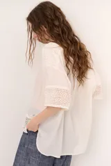 Blusa color blanco, de corte holgado y mangas tres cuartos, con detalles de encaje y bordados en las mangas y en el ruedo.