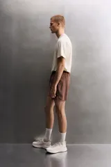 Short deportivo de entrenamiento en color marrón, confeccionado en tejido técnico ligero y elástico. Cuenta con cintura elástica ajustable con cordón, bolsillos frontales, bolsillo trasero con cierre y aberturas laterales en el bajo. Incluye un pequeño detalle de logo estampado en la pierna.