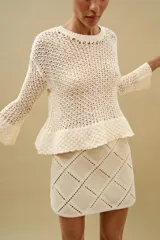 Minifalda de tiro medio confeccionada en ante color beige, decorada con aplicaciones de tejido tipo crochet blanco formando un patrón de rombos. Cuenta con cierre de cremallera oculta en la costura.