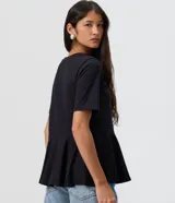 Blusa femenina de manga corta y cuello redondo, color negro, confeccionada en algodón. Presenta un corte levemente entallado con recorte en la cintura y un volado estilo peplum en el bajo.