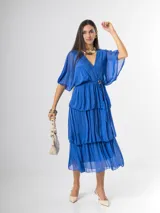 Vestido midi de seda italiana color azul, con escote en V, mangas murciélago amplias, falda de tres volados y cintura elastizada con lazo ajustable al tono y hebilla circular dorada.