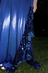 Vestido largo color azul con corte bajo el busto, escote en V y top de triángulos con lentejuelas. Presenta aberturas cut-out en la cintura, tirantes finos cruzados en la espalda y falda larga fluida con volados.