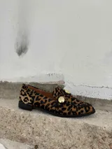 Mocasín de cuero con estampado animal print, suela plana y detalle de apliques dorados.
