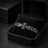 Pulsera de eslabones gruesos de acero con dije central en forma de cruz con detalles grabados.