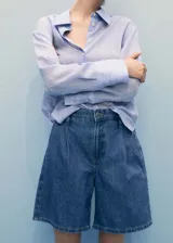 Short de denim azul de tiro medio, con diseño recto, trabillas para cinto, pinzas delanteras y cierre frontal de cremallera y botón. Cuenta con dos bolsillos laterales.