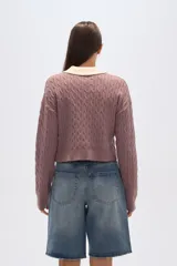 Sweater de tejido de punto con trenzas, color malva/rosado, de corte cropped y manga larga. Presenta cuello polo con solapas en color crema y cierre frontal de botones.