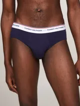 Pack de tres calzoncillos tipo slip de la marca Tommy Hilfiger, confeccionados en algodón elástico, con cintura elástica con el nombre de la marca y líneas distintivas. Incluye una unidad con cintura blanca, otra con cintura azul marino y otra con cintura roja.