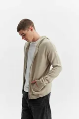 Campera de tejido de punto color beige con capucha, cierre frontal y bolsillos delanteros, de corte oversize y hombros caídos.