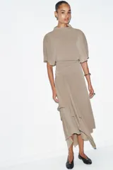 Top fluido color beige, con cuello perkins y mangas por debajo del codo. Bajo redondeado.