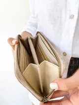 Billetera grande de cuero con diseño bicolor en tonos beige y crema, con textura grabada en el cuerpo principal y detalles en cuero liso. Cuenta con cierre perimetral metálico y tirador de cuero.