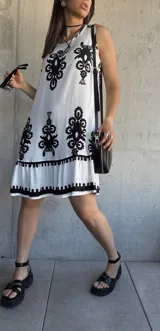 Vestido corto blanco con estampado de flores negras, corte suelto y ruedo con volantes.