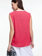 Chaleco sin mangas color coral, con escote en V, cierre frontal con botones de madera y bolsillos de parche. Incluye tres pins decorativos: un corazón plateado, un círculo plateado y un cuadrado rojo. Confeccionado en tejido liviano de lino y viscosa.