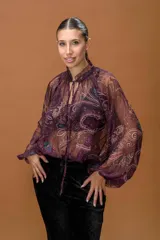 Blusa de gasa translúcida con estampado paisley en tonos burdeos, beige y azul. Presenta cuello alto con volantes, abertura frontal con cordones ajustables y mangas largas abullonadas con puños elásticos.