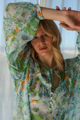 Blusa estampada en tonos de verde, celeste y amarillo, con sutiles hilos de lurex dorados. Cuello con lazo y abotonadura, y corte en el pecho con fruncido.