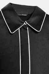 Camisa de corte amplio confeccionada en tejido satinado, con cuello solapa y manga larga. Presenta detalles de vivos en contraste y cierre frontal con botones ocultos.