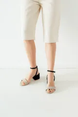 Sandalias de tacón bajo cuadrado, con tira delantera en color beige y pulsera al tobillo en color negro con cierre de hebilla.