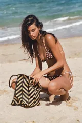 Bolso tipo shopper de yute 100%, con diseño de rayas y chevron en tonos negro y tostado, asas de hombro trenzadas y forma trapezoidal.