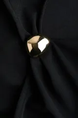Musculosa negra confeccionada en punto de crepé, con diseño sin mangas, elegante escote drapeado y un aplique metálico dorado decorativo en el hombro derecho.