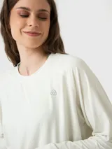 Polera de manga larga en color blanco hueso, confeccionada en tejido suave y ligero. Presenta cuello redondo, puños elásticos y ajuste en la cintura, con un pequeño logo bordado en el pecho.