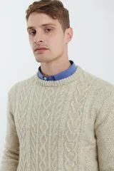 Sweater de tejido de punto color beige claro, con diseño de trenzas (aranes) en el frente y mangas de punto liso. Tiene cuello redondo.