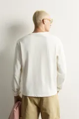 Camiseta relaxed fit de color blanco off-white, confeccionada en tejido texturizado con estructura. Presenta cuello redondo y manga larga.