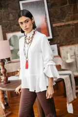 Blusa blanca de textura arrugada, con cuello alto, abertura frontal tipo gota y mangas largas acampanadas con detalle de frunces.